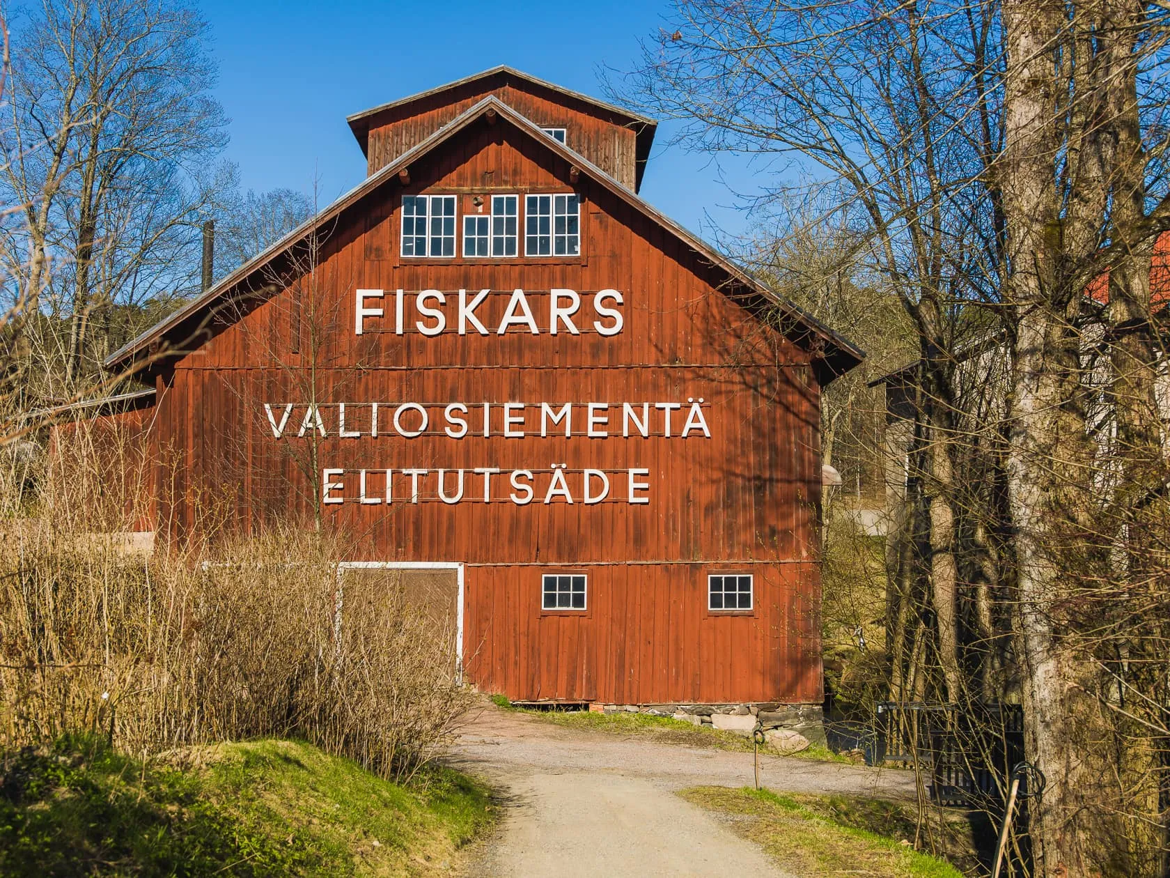 Красный деревянный амбар с надписью FISKARS среди деревьев