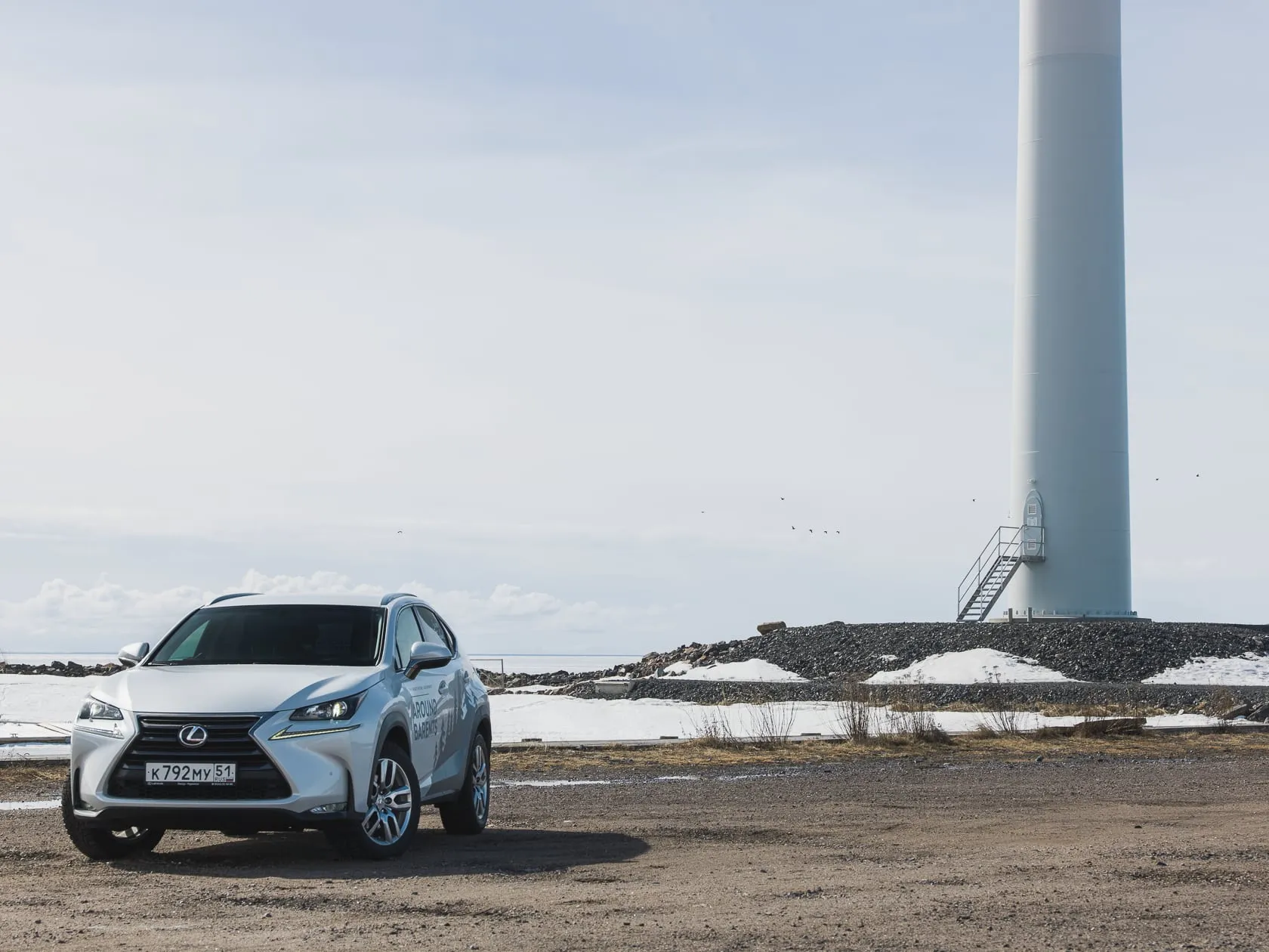 Белый внедорожник Lexus у подножия ветряной турбины на берегу