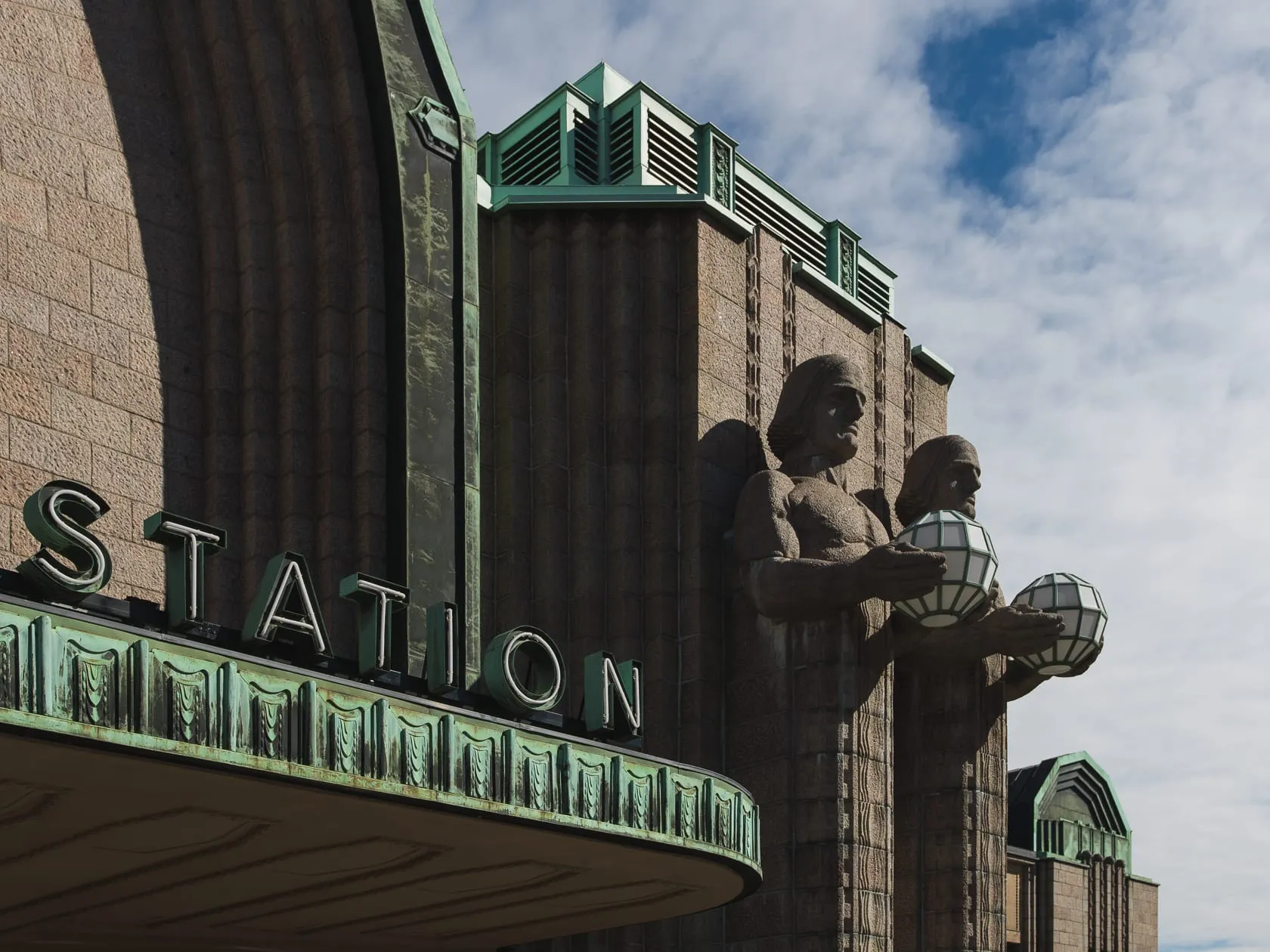 Каменные фигуры с фонарями и надпись STATION на фасаде вокзала
