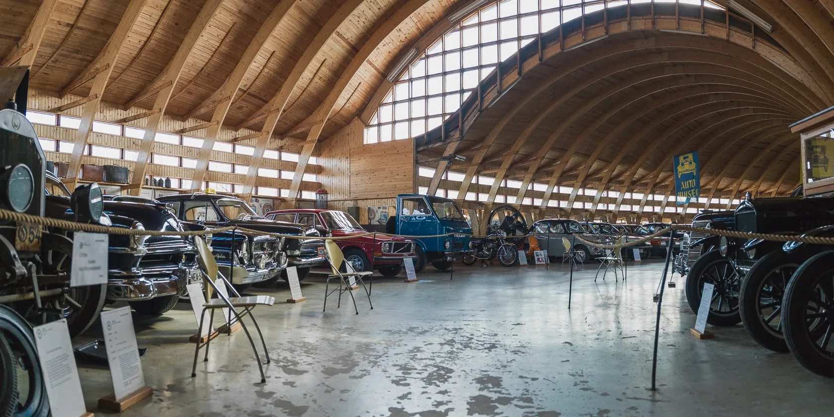 Ряды старинных автомобилей в ангаре с деревянным сводчатым потолком