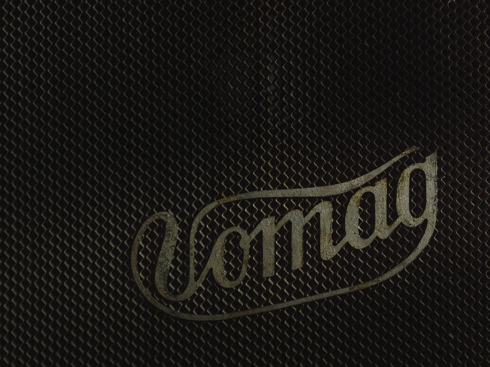 Логотип Vomag на тёмной сетчатой решётке радиатора крупным планом