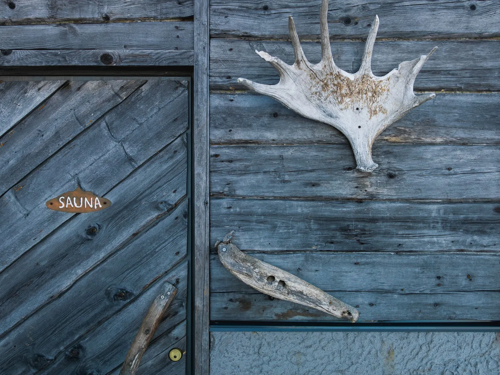 Деревянная стена бани с табличкой SAUNA и лосиными рогами