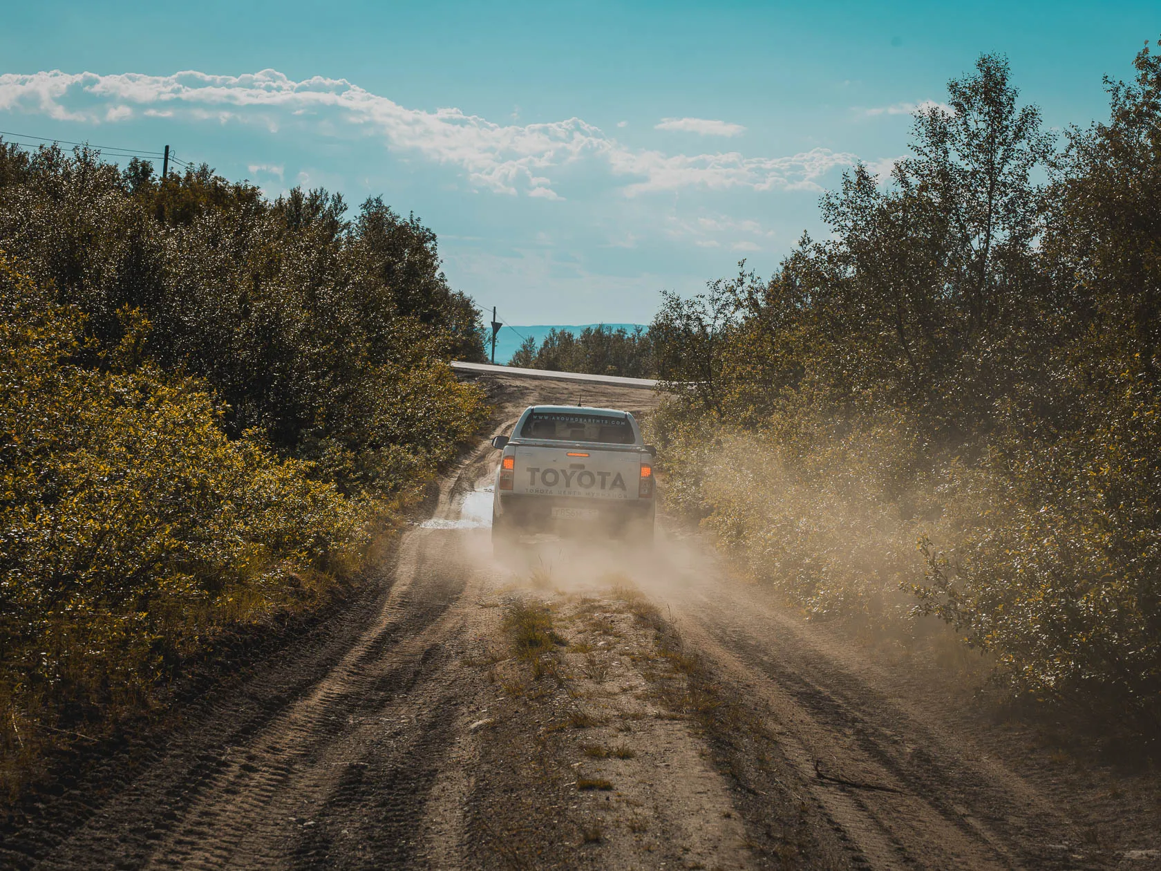 Автомобиль Toyota поднимает пыль на грунтовой лесной дороге