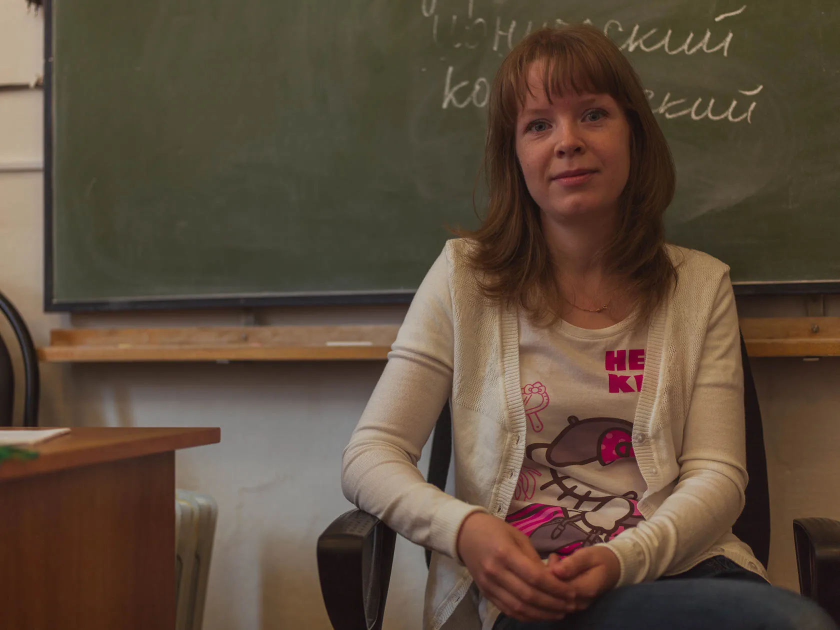 Молодая женщина сидит у школьной доски в классе