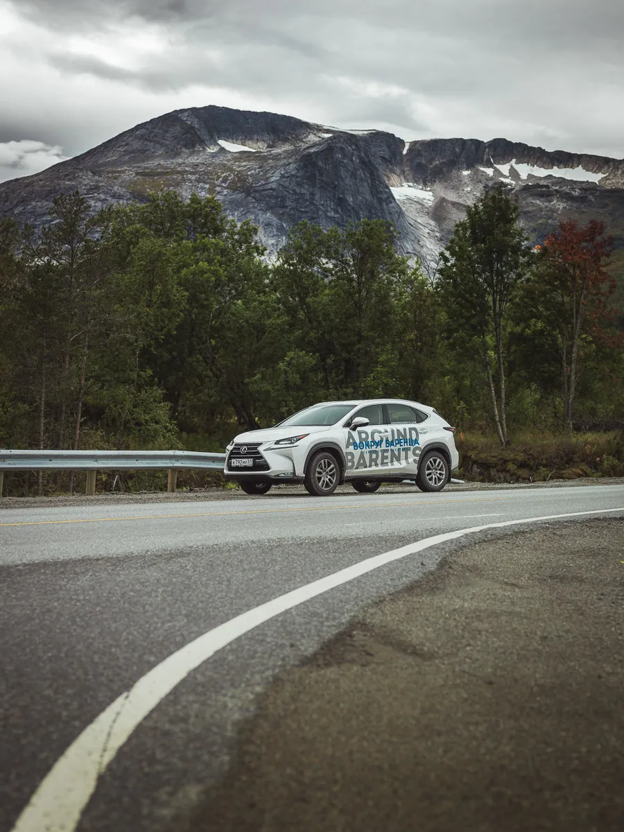 Белый внедорожник с надписью Around Barents у дороги на фоне горы с ледником